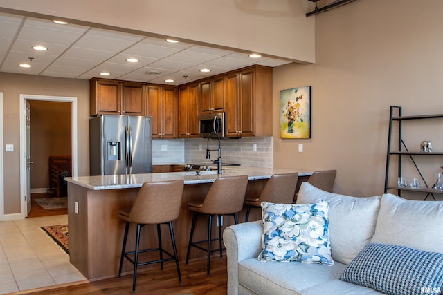 kitchen with a kitchen breakfast bar, light stone counters, kitchen peninsula, and appliances with stainless steel finishes