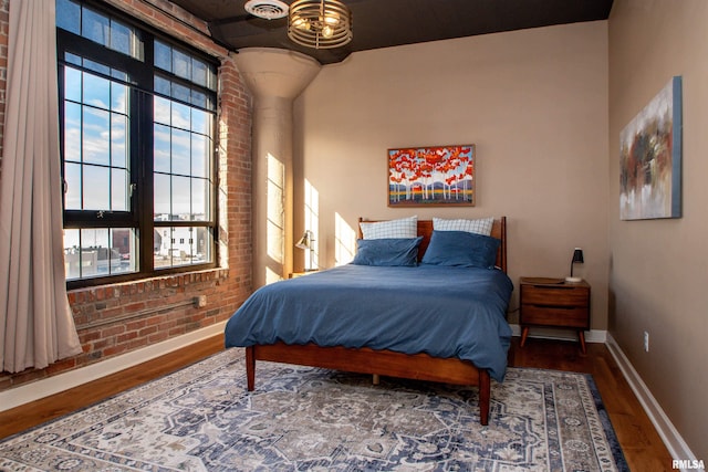 bedroom featuring brick wall and hardwood / wood-style flooring