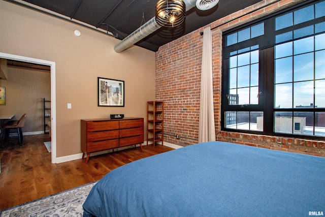 bedroom with dark wood-type flooring and brick wall