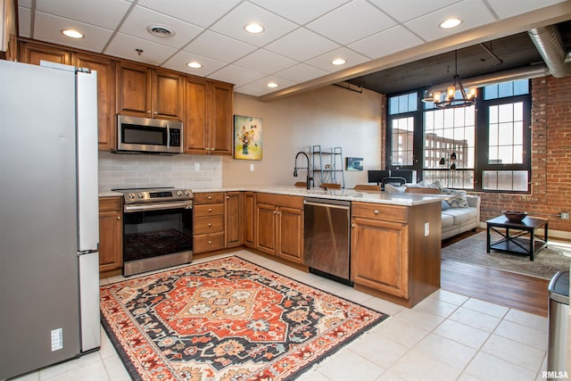 kitchen featuring light tile patterned floors, appliances with stainless steel finishes, a notable chandelier, kitchen peninsula, and brick wall