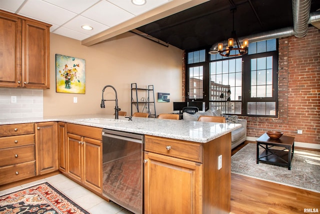 kitchen with kitchen peninsula, brick wall, sink, dishwasher, and a chandelier