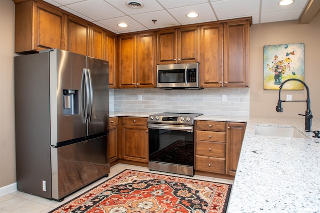 kitchen with backsplash, sink, light tile patterned floors, light stone countertops, and appliances with stainless steel finishes