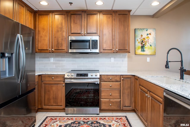 kitchen featuring light stone countertops, appliances with stainless steel finishes, backsplash, sink, and light tile patterned floors