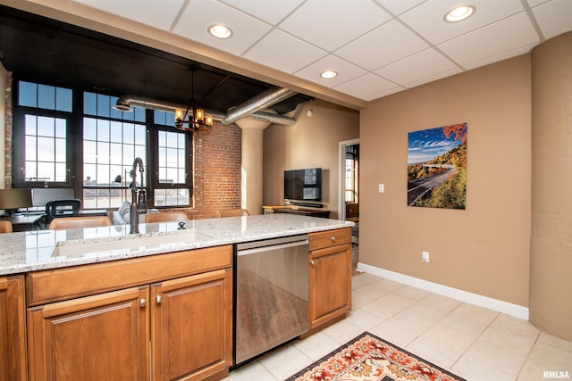 kitchen with light stone counters, sink, stainless steel dishwasher, and a notable chandelier