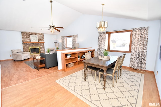 dining area with lofted ceiling, ceiling fan with notable chandelier, a fireplace, wood finished floors, and baseboards