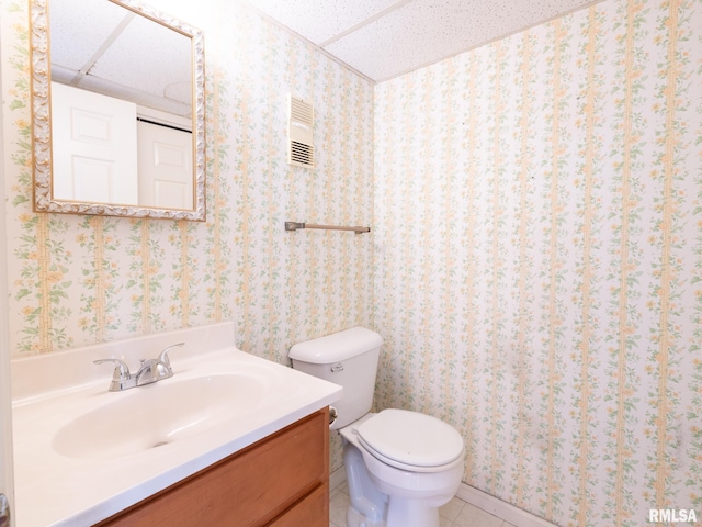 bathroom with toilet, vanity, tile patterned floors, and a drop ceiling