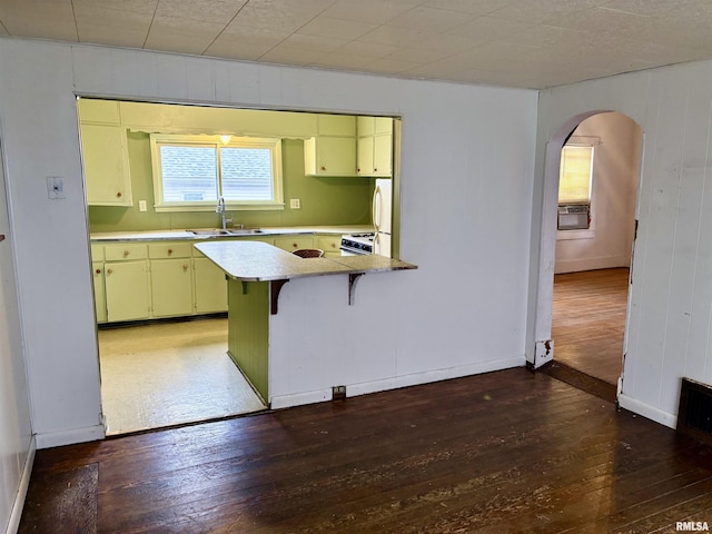 kitchen with kitchen peninsula, a kitchen bar, dark hardwood / wood-style flooring, sink, and wood walls