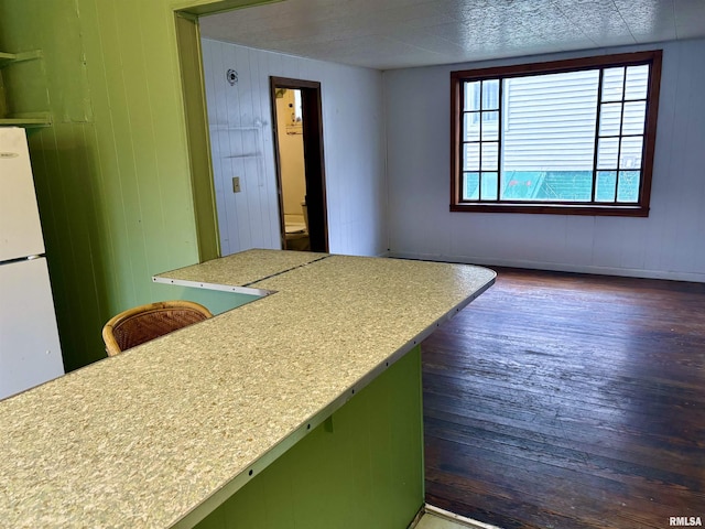 kitchen with wood walls, a kitchen breakfast bar, green cabinets, white refrigerator, and dark hardwood / wood-style floors