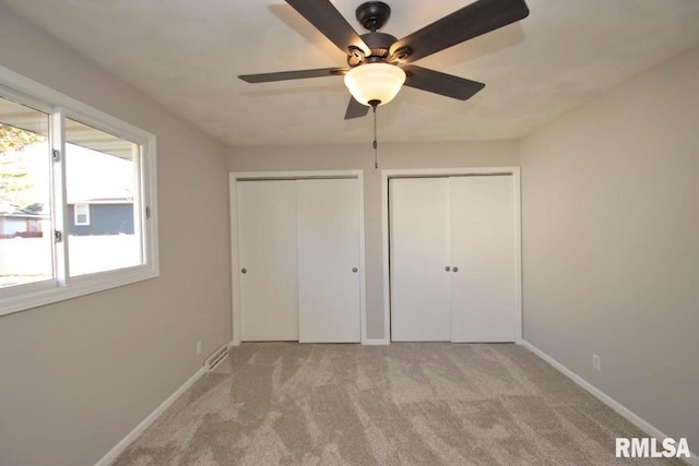 unfurnished bedroom featuring ceiling fan, light carpet, and multiple closets