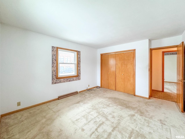 unfurnished bedroom with light carpet, a closet, and a baseboard heating unit