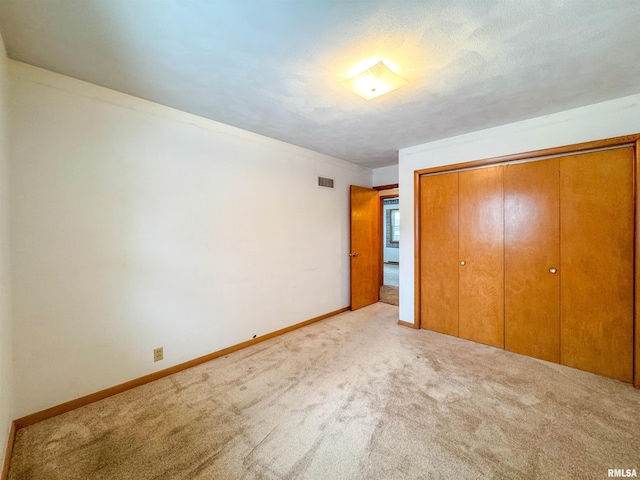 unfurnished bedroom with light carpet, a textured ceiling, and a closet