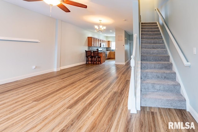 stairs featuring ceiling fan with notable chandelier and hardwood / wood-style flooring