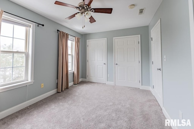 unfurnished bedroom featuring multiple windows, ceiling fan, light colored carpet, and multiple closets