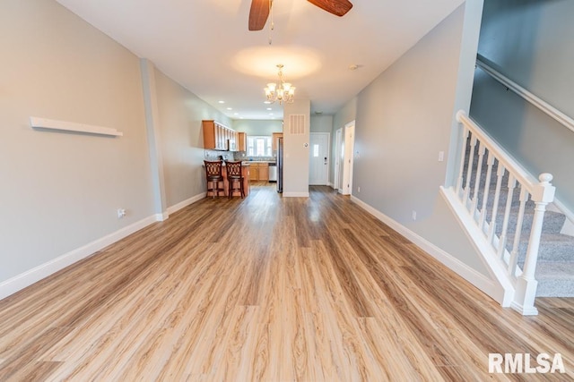 unfurnished living room with ceiling fan with notable chandelier and light hardwood / wood-style floors