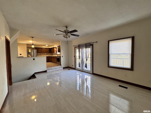 unfurnished living room featuring ceiling fan, plenty of natural light, light tile patterned flooring, and a textured ceiling