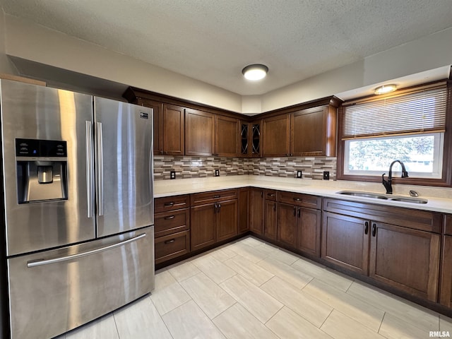 kitchen featuring dark brown cabinetry, sink, tasteful backsplash, stainless steel refrigerator with ice dispenser, and a textured ceiling