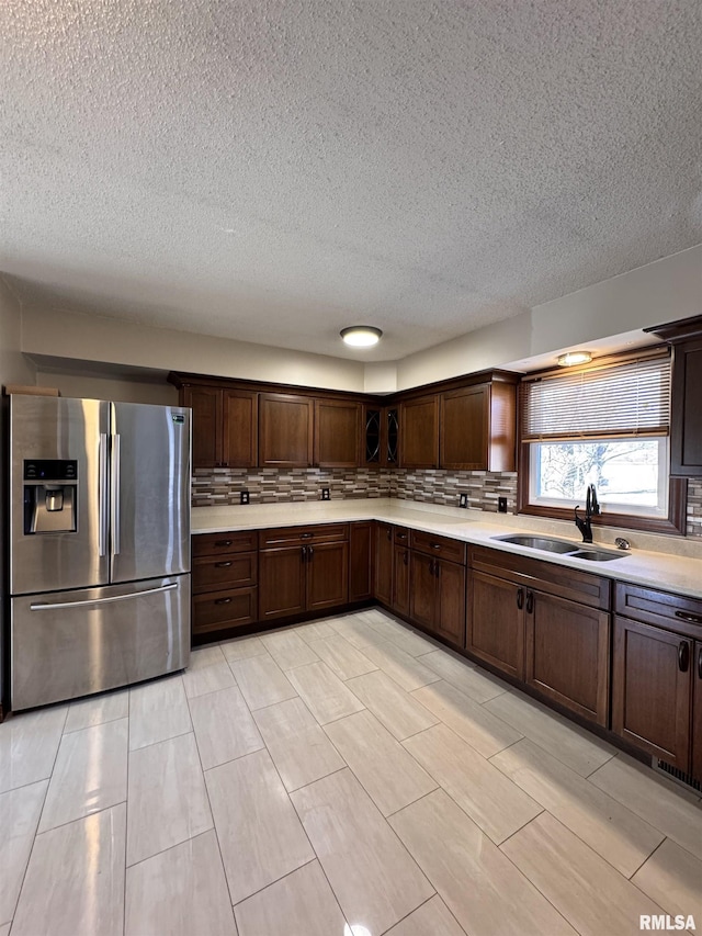 kitchen with sink, stainless steel refrigerator with ice dispenser, a textured ceiling, decorative backsplash, and dark brown cabinets