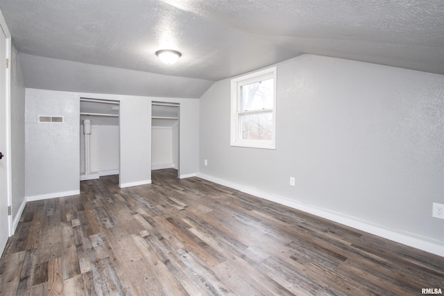 unfurnished bedroom with a textured ceiling, dark hardwood / wood-style floors, vaulted ceiling, and multiple closets