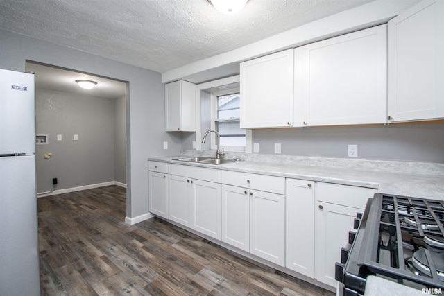 kitchen featuring white refrigerator, white cabinetry, sink, and stainless steel range