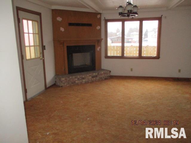 unfurnished living room featuring a fireplace, carpet, an inviting chandelier, and crown molding