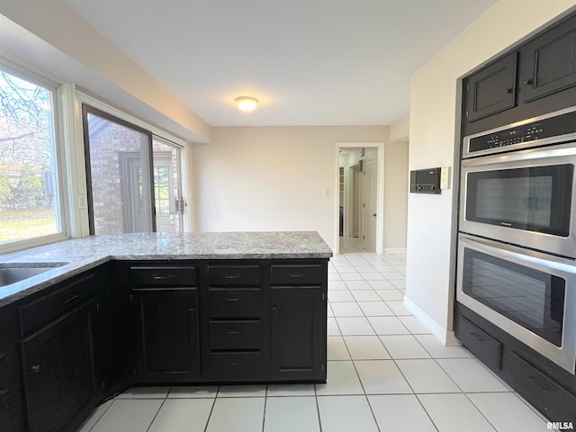 kitchen featuring light stone counters, stainless steel double oven, sink, and light tile patterned floors