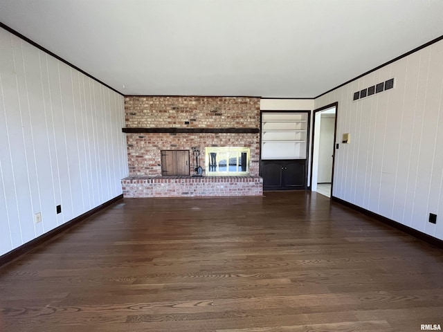 unfurnished living room featuring a fireplace, crown molding, dark wood-type flooring, and wooden walls