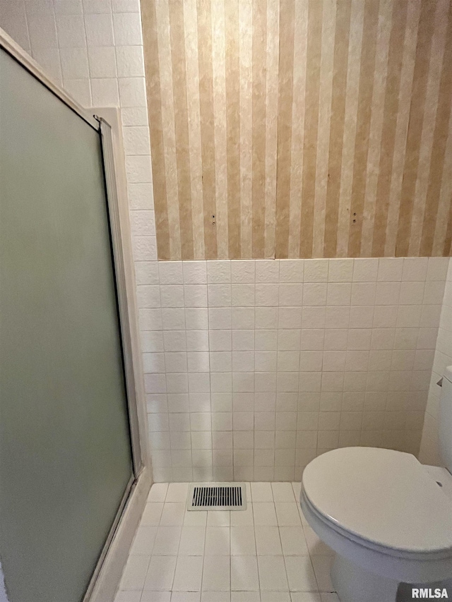 bathroom with tile patterned flooring, toilet, tile walls, and an enclosed shower