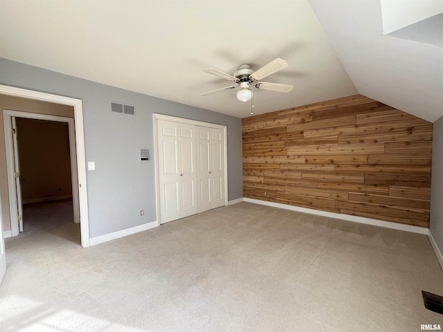 unfurnished bedroom with light colored carpet, ceiling fan, a closet, lofted ceiling, and wood walls