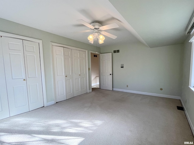 unfurnished bedroom featuring light carpet, two closets, and ceiling fan