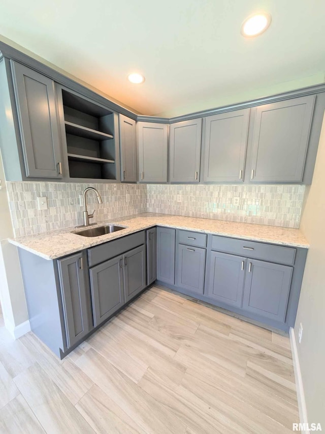 kitchen with backsplash, gray cabinets, light stone countertops, and sink