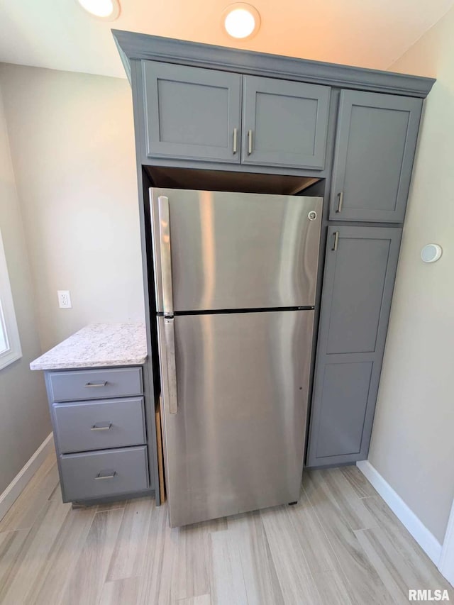 kitchen with gray cabinets, light hardwood / wood-style floors, light stone countertops, and stainless steel refrigerator