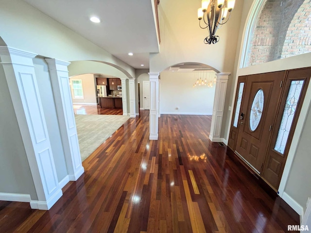 entrance foyer with ornate columns, dark hardwood / wood-style floors, a high ceiling, and an inviting chandelier