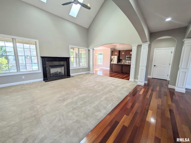 unfurnished living room with high vaulted ceiling, a skylight, ceiling fan, a premium fireplace, and dark hardwood / wood-style flooring