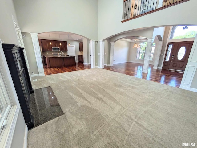 unfurnished living room featuring decorative columns, dark hardwood / wood-style floors, a high ceiling, and an inviting chandelier