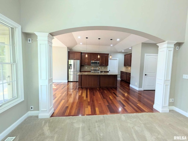 kitchen with stainless steel appliances, hanging light fixtures, dark wood-type flooring, and an island with sink