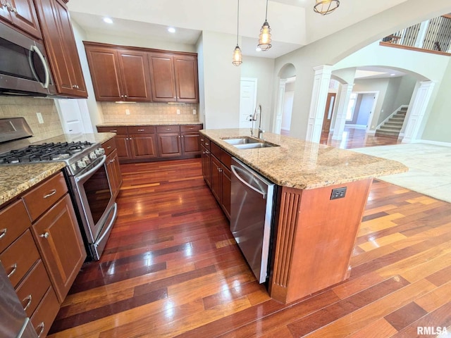 kitchen with appliances with stainless steel finishes, tasteful backsplash, sink, dark hardwood / wood-style floors, and an island with sink