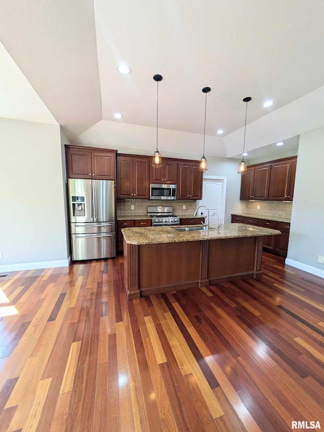 kitchen featuring pendant lighting, backsplash, dark wood-type flooring, light stone countertops, and appliances with stainless steel finishes