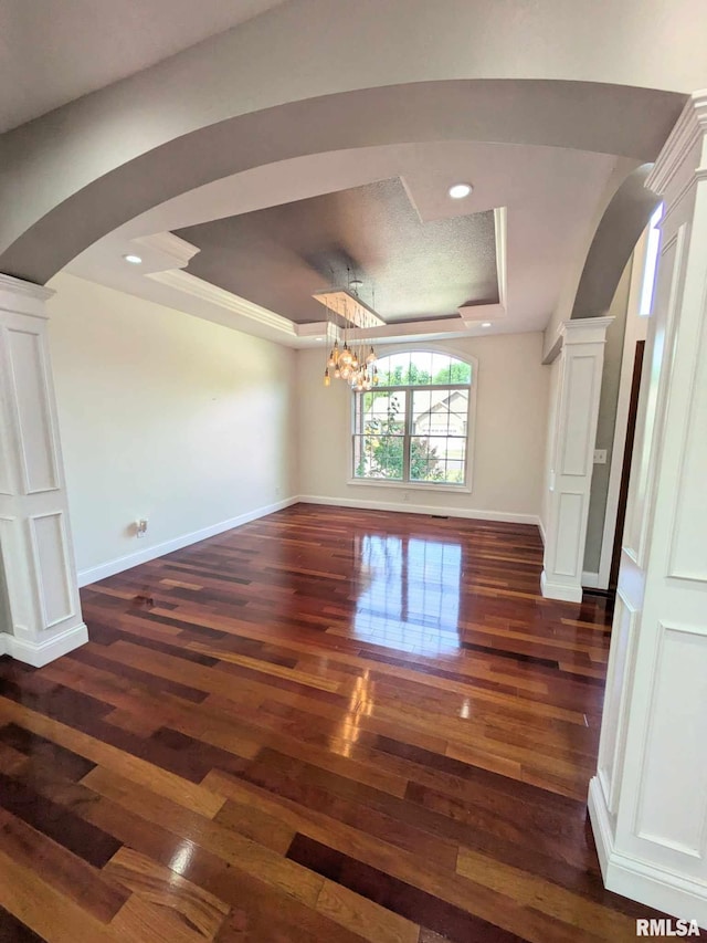 spare room featuring a chandelier, a tray ceiling, crown molding, and dark wood-type flooring