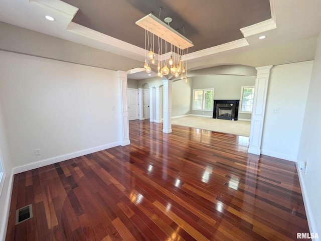 unfurnished dining area featuring a multi sided fireplace, a tray ceiling, dark wood-type flooring, and a notable chandelier