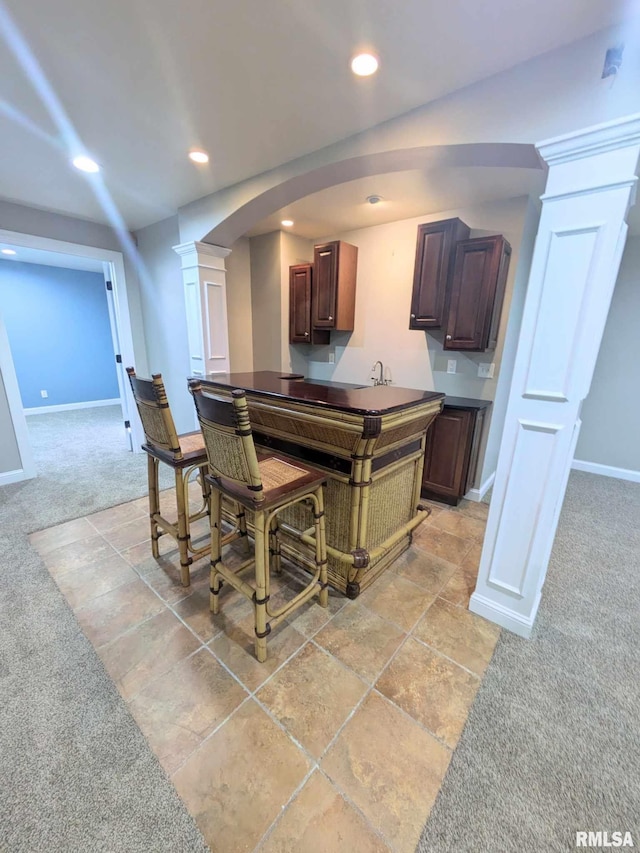 kitchen featuring a kitchen breakfast bar, light colored carpet, decorative columns, and sink