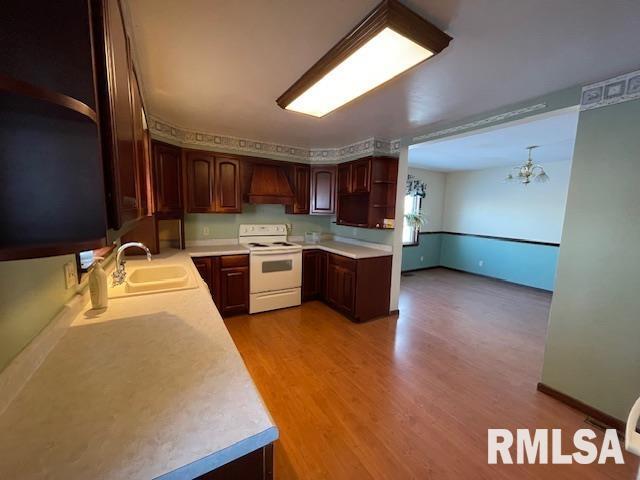 kitchen featuring light wood-type flooring, custom range hood, white range with electric stovetop, sink, and an inviting chandelier