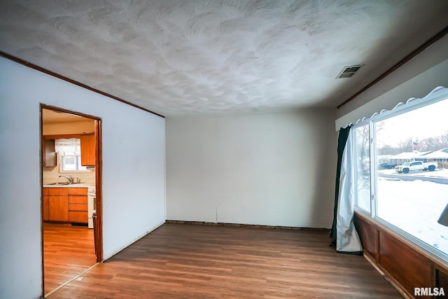 unfurnished room with hardwood / wood-style floors, ornamental molding, a textured ceiling, and sink