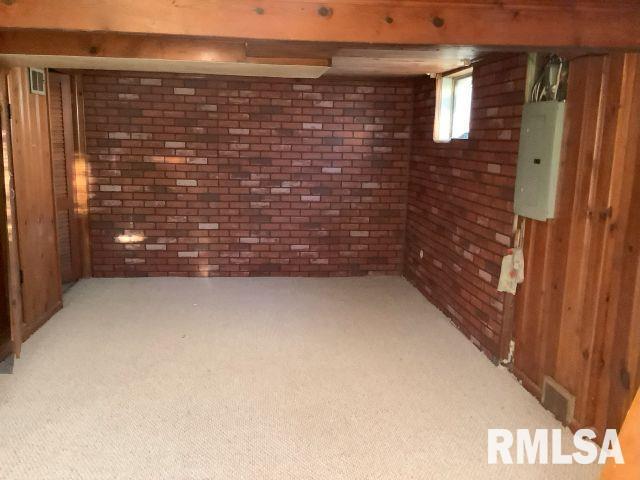 basement featuring electric panel, carpet floors, and brick wall