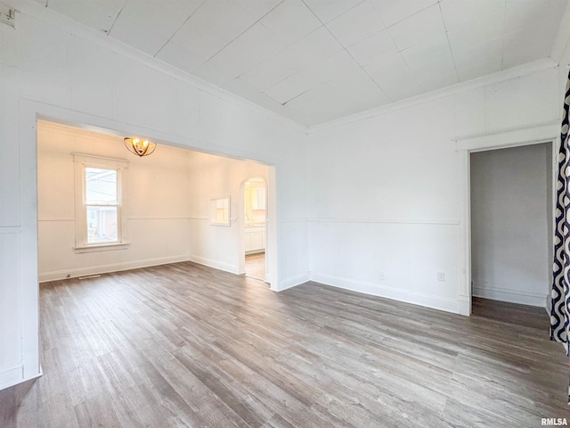 unfurnished room with wood-type flooring, crown molding, and a notable chandelier