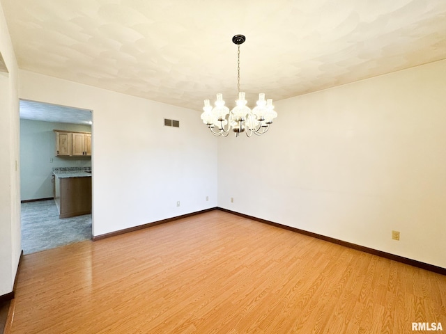 empty room with a chandelier and light hardwood / wood-style floors