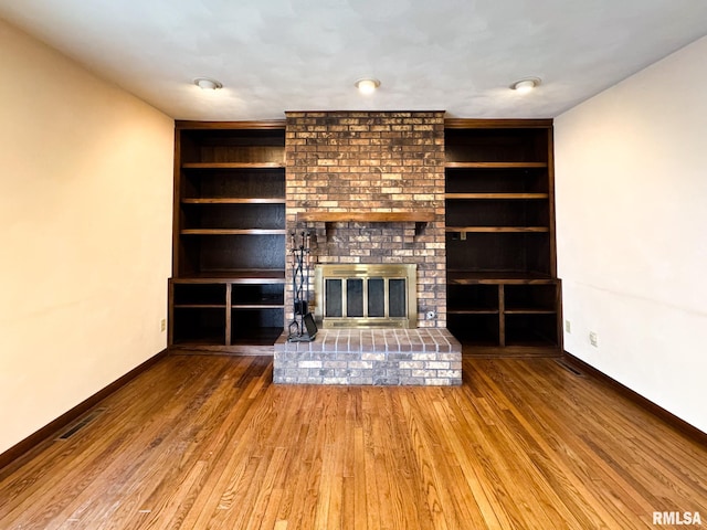 unfurnished living room with built in features, a brick fireplace, and wood-type flooring