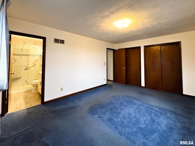 unfurnished bedroom featuring carpet, connected bathroom, a textured ceiling, and two closets