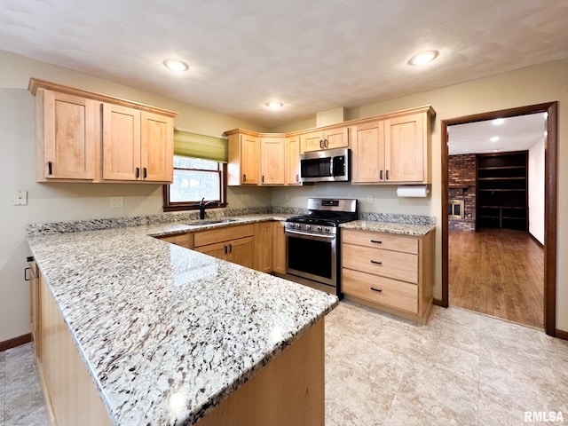 kitchen featuring light stone countertops, appliances with stainless steel finishes, sink, kitchen peninsula, and light brown cabinets