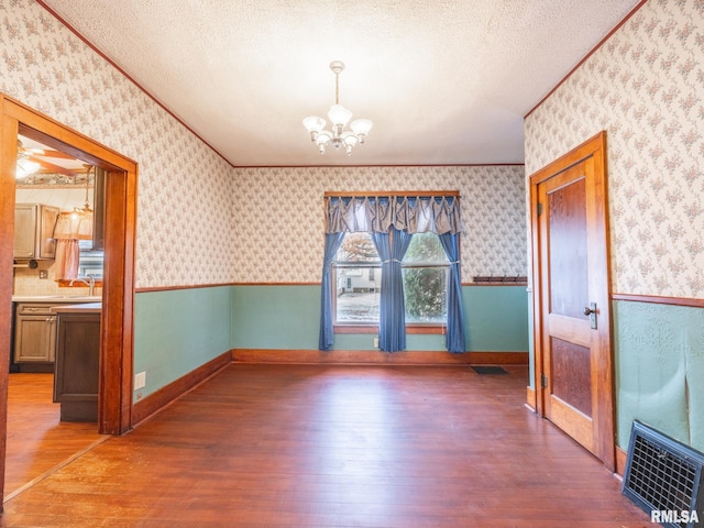 unfurnished dining area with sink, a notable chandelier, dark hardwood / wood-style flooring, and a textured ceiling