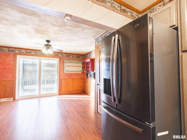 kitchen featuring hardwood / wood-style floors, ceiling fan, stainless steel fridge with ice dispenser, and wooden walls